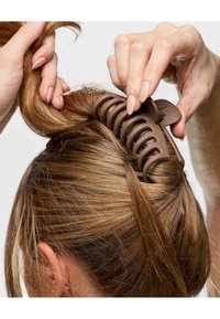 Brauner Kunststoffhaarklammer greift lange, glatte Haare, mit einem weit offenen Design und mehreren gebogenen Zähnen für einen sicheren Halt.