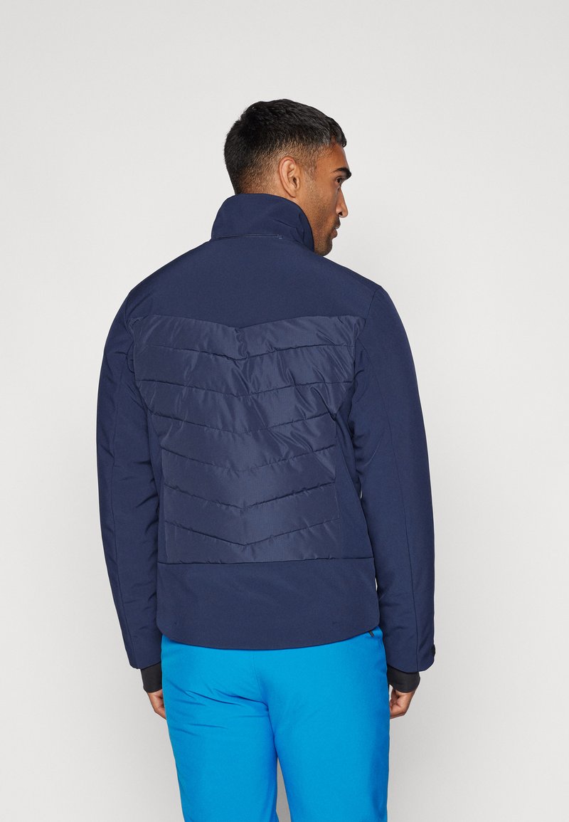 Donkerblauwe pufferjack met een hoge kraag, voorzien van een chevron gestikte patroon op de rug en contrasterende mouwboorden.