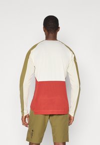 Maglietta sportiva a maniche lunghe con un design a blocchi di colore in crema, verde oliva e rosso. Realizzata in un tessuto testurizzato e traspirante, con maniche raglan.
