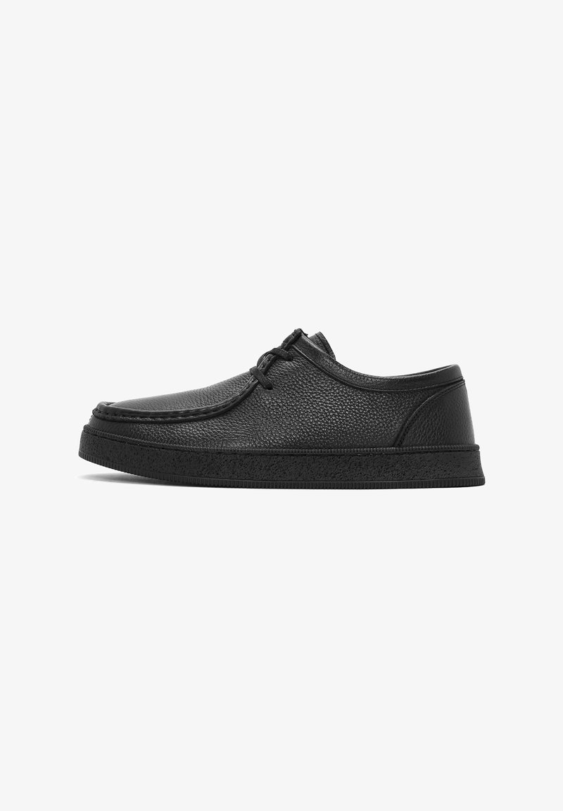 Chaussure décontractée en cuir noir texturé avec laçage à l'avant et semelle épaisse en caoutchouc, vue de profil sur fond blanc.