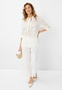 Weiße Augenbluse mit einer Schleife, Dreiviertelärmel und gewelltem Saum. Kombiniert mit weißen weiten Hosen mit Spitzenakzenten.
