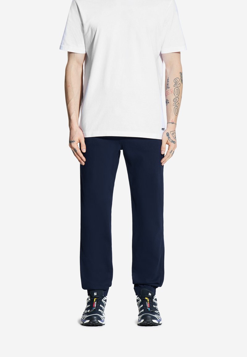 Granatowe joggerki z elastycznymi mankietami, w zestawieniu z białą koszulką z krótkim rękawem. Czarne i kolorowe buty sportowe dopełniają strój.