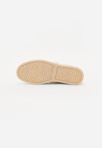 Suela de zapato color beige claro con un patrón de diamante, material de goma texturizado, con el logo "TOMS" grabado y forma de punta redondeada.
