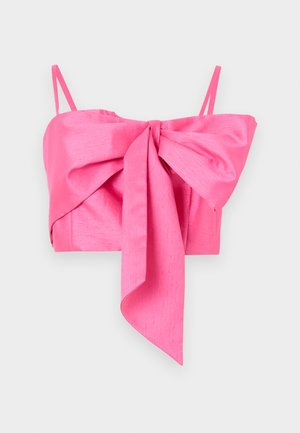Un crop top en satin rose avec un grand nœud, associé à un jean en denim noir taille haute et des escarpins noirs à talons pointus ; un petit sac à main noir minimaliste.