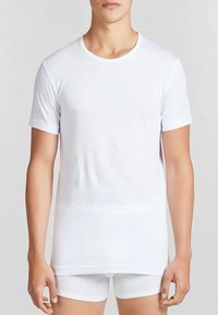 T-shirt bianca a maniche corte realizzata in tessuto liscio, con scollatura rotonda e vestibilità regolare. Indossata su pantaloni corti bianchi aderenti.