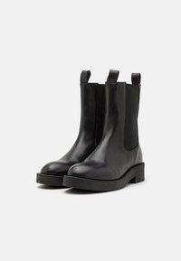 Bottines en cuir noir avec des panneaux élastiques sur les côtés, bouts ronds et languettes de tirage. Semelles en caoutchouc plates avec une finition texturée.