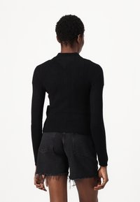 Svart strikket genser med ribbet tekstur og lange ermer. Har en rund halslinning og en tettsittende design. Brukes med opprevne svarte denimshorts.