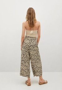Haut court beige en crochet avec un pompon, associé à un pantalon large à imprimé animalier beige et noir, porté avec des sandales légères.