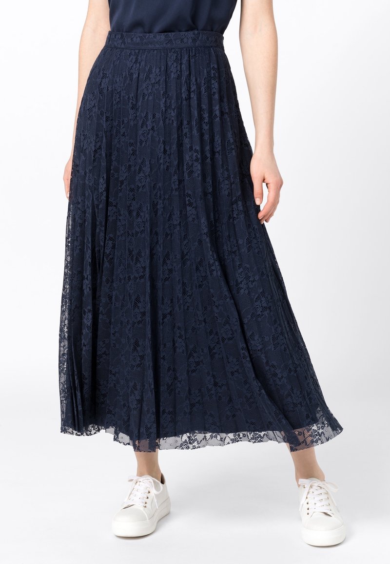Námořnicky modrá plisovaná maxi sukně z krajky s texturovaným vzorem, se střiženým pasem a průhledným lemem, doplněná bílými teniskami.