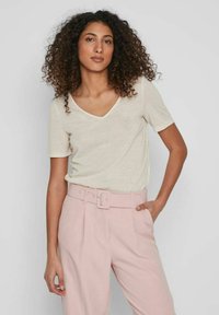 Tricou bej cu decolteu în V, asortat cu pantaloni roz deschis cu talie înaltă, având o curea lată și o cataramă. Textură netedă din bumbac, cu mâneci scurte.