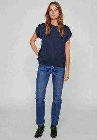 Top de manga curta azul-marinho com um corte descontraído, combinado com jeans retos azul-claro e botas de tornozelo pretas. Tecido liso e suave.