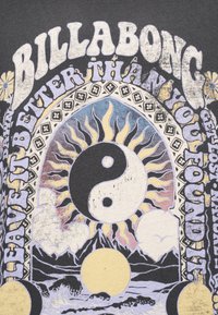 Κείμενο Billabong με ήλιο και φεγγάρι, σύμβολο γιν-γιανγκ, βουνά, κύματα, σύννεφα και λουλούδια σε παστέλ αποχρώσεις σε σκουρόχρωμο φόντο υφάσματος.