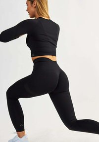 Completo sportivo nero composto da un top cropped a maniche lunghe e leggings a vita alta. Il tessuto ha una consistenza liscia e elastica con un discreto dettaglio del logo.