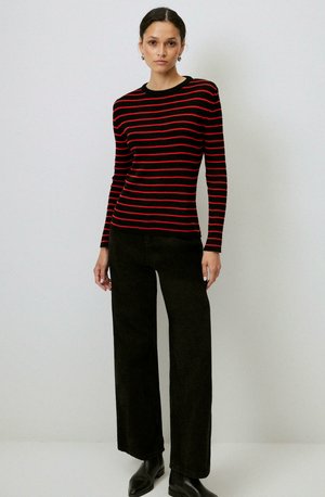 Pull rayé noir et rouge, à côtes, à manches longues, avec un col rond, associé à un pantalon large taille haute noir et des bottines.