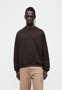 Sweat-shirt marron en coton, avec un col rond et des poignets côtelés. Détail logo sur la poitrine, associé à un pantalon texturé beige clair.