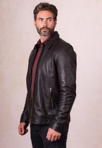 Black leather jacket with a stand collar, front zip closure, and two side zip pockets. Smooth texture and tailored fit.