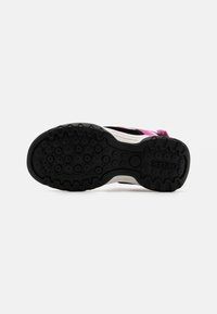 Black rubber sneaker sole with circular patterns. Features a white midsole and pink accents on the upper section, designed for traction.