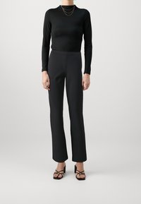 Maglietta nera a maniche lunghe abbinata a pantaloni neri a vita alta, con una texture liscia e un design semplice e aderente, completata da tacchi neri con cinturini.