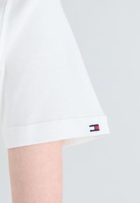 Hvit bomull t-skjorte med ribbestrikket kant på ermene, utstyrt med en liten flerfarget flagglogo på mansjetten. Myk tekstur med en klassisk passform.