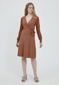 Rostfärgad, ribbad omlottskjerfklänning med lång ärm och knytning vid midjan. Bärs med ljusgrå, kraftiga klacksandaler.