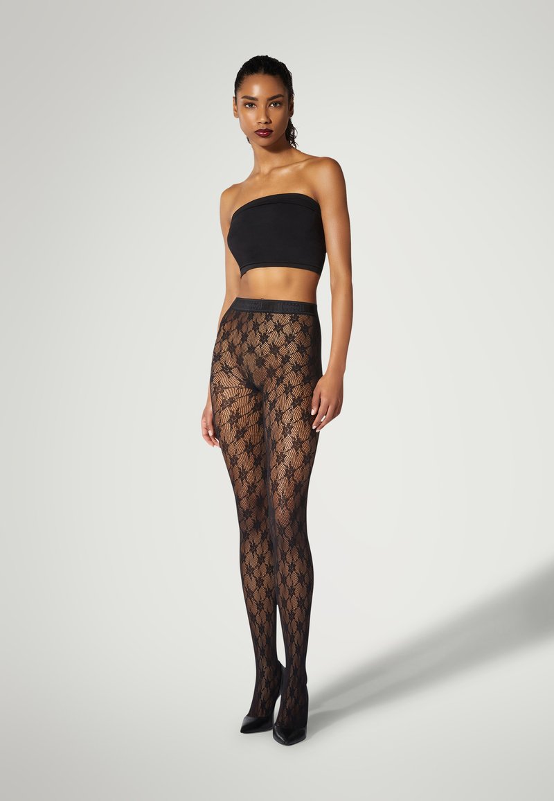 Collant neri in pizzo con un motivo floreale, caratterizzati da una texture trasparente e una vita liscia. Abbinati a un top nero senza spalline e tacchi.