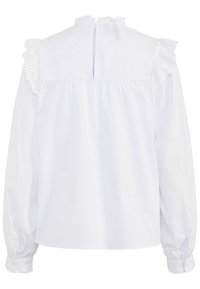 Blouse blanche avec des accents de volants aux épaules, col haut et fermeture à boutons à l'arrière. Fabriquée dans un tissu lisse, avec des manches longues et froncées.