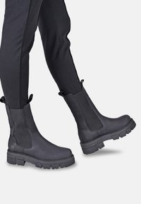 Black Chelsea boots featuring smooth leather with elastic side panels and durable rubber soles, showcasing a textured finish and a lug sole design.