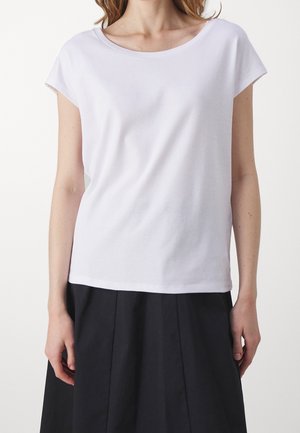 Mujer que lleva una camiseta blanca lisa de manga corta metida en una falda negra de cintura alta, vista desde el cuello hasta las caderas.