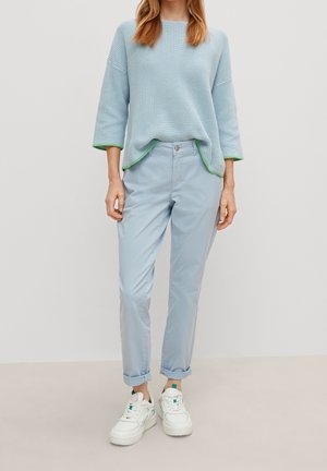 Lichtblauwe gebreide trui met groene bies, gecombineerd met lichtblauwe broek en witte sneakers. Relaxte pasvorm, zachte textuur, omgeslagen manchetten.