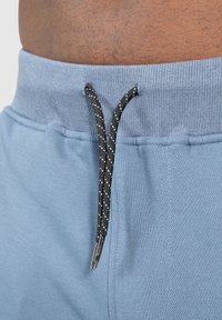 Světlé modré sportovní šortky s texturovanou tkaninou, elastickým pasem a černým šňůrkovým zavazováním s bílými akcenty.