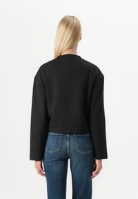 Musta cropped-huppari, jossa on pitkät hihat, pyöreä pääntie ja sileä pinta. Yhdistetty sinisiin farkkuihin, joissa on takataskut.