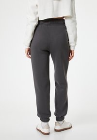 Mørkegrå joggere med elastisk linning og ankelmanchetter, lavet af et blødt materiale, parret med hvide sneakers og ribbede sokker.