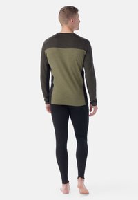 Olive green long-sleeved top with darker green shoulder panel, paired with black leggings. Smooth texture, fitted design.
