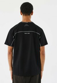 Camiseta negra de manga corta, con el texto "PROJECT X PARIS" y detalles grises en la parte superior de la espalda y el cuello. Textura suave.