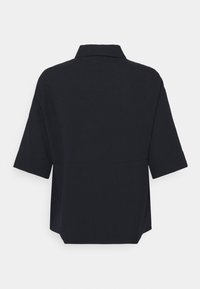 Chemise noire à manches courtes texturée avec un col, présentée de dos sur un fond blanc uni.
