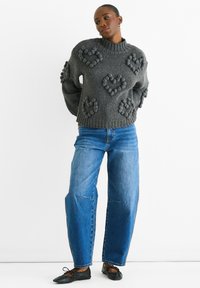 Maglione grigio a maglia con motivi a cuore a bolle, colletto alto e spalle cadenti, abbinato a jeans blue dritti e ballerine nere.