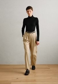 Jersey negro de cuello alto, pantalones de tiro alto beige con pliegues, y mocasines negros. Diseño simple con una paleta de colores neutros y un ajuste a medida.