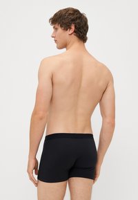 Černé boxerky s měkkým pasem, vyrobené z elastického bavlněného materiálu, s přiléhavým střihem a hladkou texturou. Mají minimalistický styl bez vzorů.