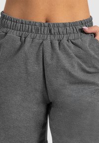Grijze sweatpants met een elastische tailleband, zachte textuur en zijzakken. Een klein logo is geborduurd op de linkerdij.
