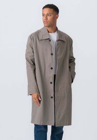 Gr�å knælang frakke med krave, knaplukning foran og lange ærmer. Materialet ser glat og struktureret ud. Bæres over en hvid skjorte.