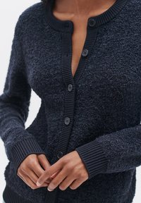 Cardigan blu navy con tessuto texturizzato, colletto e polsini a coste, e sei bottoni prominenti sul davanti.