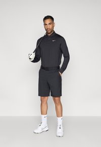 Μαύρο μπλουζάκι πόλο με μακριά μανίκια και γιακά, μαύρο σορτς, λευκά γάντια γκολφ και λευκά παπούτσια. Λογότυπο Nike στο μπλουζάκι και τις κάλτσες.