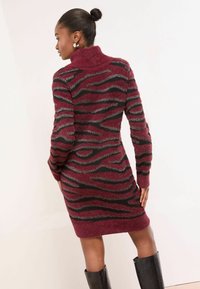 Sukienka z golfem dzianinowa w kolorze burgundowym z czarnymi i srebrnymi falistymi wzorami. Miękka tekstura, długie rękawy i dopasowany krój.