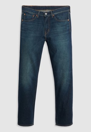 Jean droit bleu foncé avec cinq poches, rivets en cuivre et coutures orange visibles sur un fond gris clair.