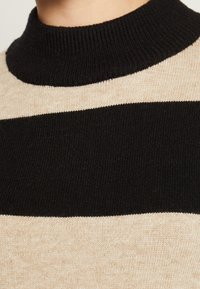 Chunky stickad tröja i beige och svarta ränder, med en hög ribbad krage. Den mjuka texturen med kontrasterande färger skapar en djärv design.