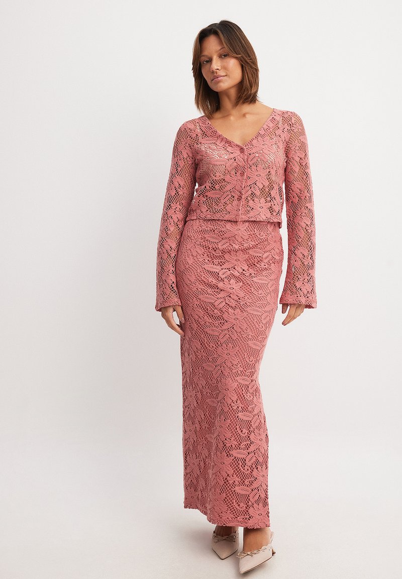 Lace dress set in dusty pink, featuring a cropped cardigan and long skirt with floral patterns, complementing fitted design and textured finish.