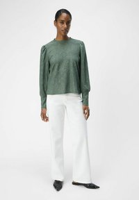 Grön texturerad blus med puffärmar och rund halsringning, kombinerad med vita vida jeans och svarta spetsiga ballerinas.