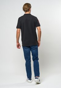 Černé polo tričko s límcem, krátkými rukávy a červenými doplňky; doplněné modrými džínami a bílými teniskami. Hladká textura látky.