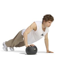 Jeune homme effectuant une pompe avec une main sur un ballon médicinal noir Adidas et l'autre au sol.
