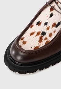 Shoe din piele maro cu vârful din piele de vacă bej și maro cu pături, talpa din cauciuc negru contrastant, caracterizându-se printr-un vârf rotunjit și detalii cu șireturi.